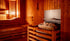 Holzsauna mit hellen Bänken und einem Saunaofen mit Steinen in der Ecke.