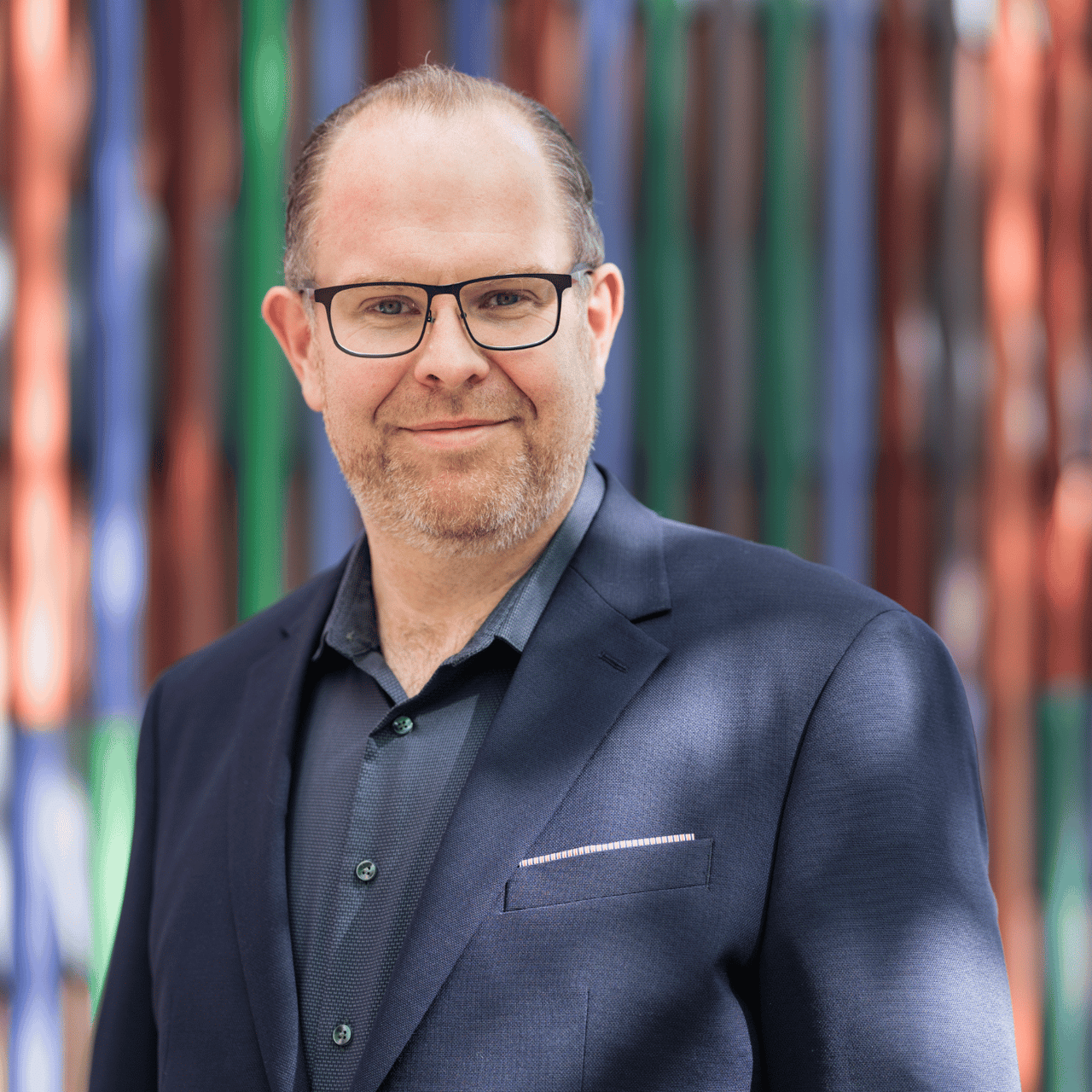 Lächelnder Mann mit Brille und grauem Hemd blickt in die Kamera.
