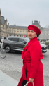 Frau in rotem Mantel und Barett steht vor dem Louvre in Paris.