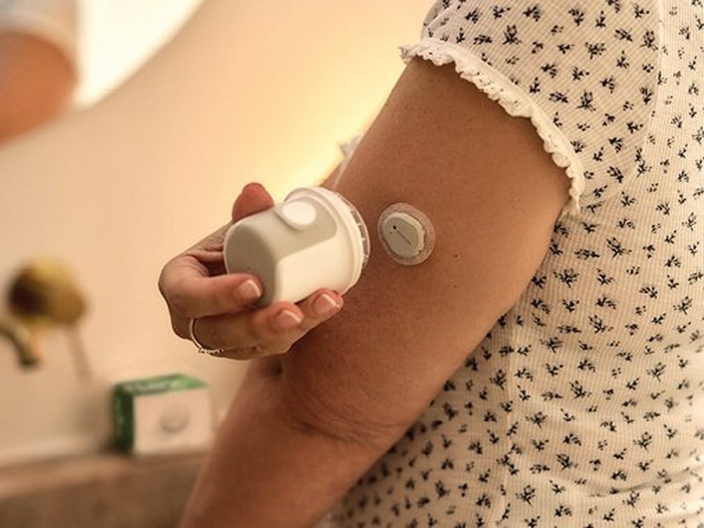 Frau bringt den Dexcom Flex Sensor mit dem Applikator am Oberarm an