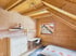 Schlafzimmer im Dachgeschoss mit Holzdecke, Schreibtisch, weißer Kommode und Bett unter einer Dachschräge.