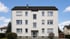 Dreistöckiges weißes Mehrfamilienhaus mit Satteldach, zentralem Eingangsbereich und symmetrischen Fenstern vor blauem Himmel.