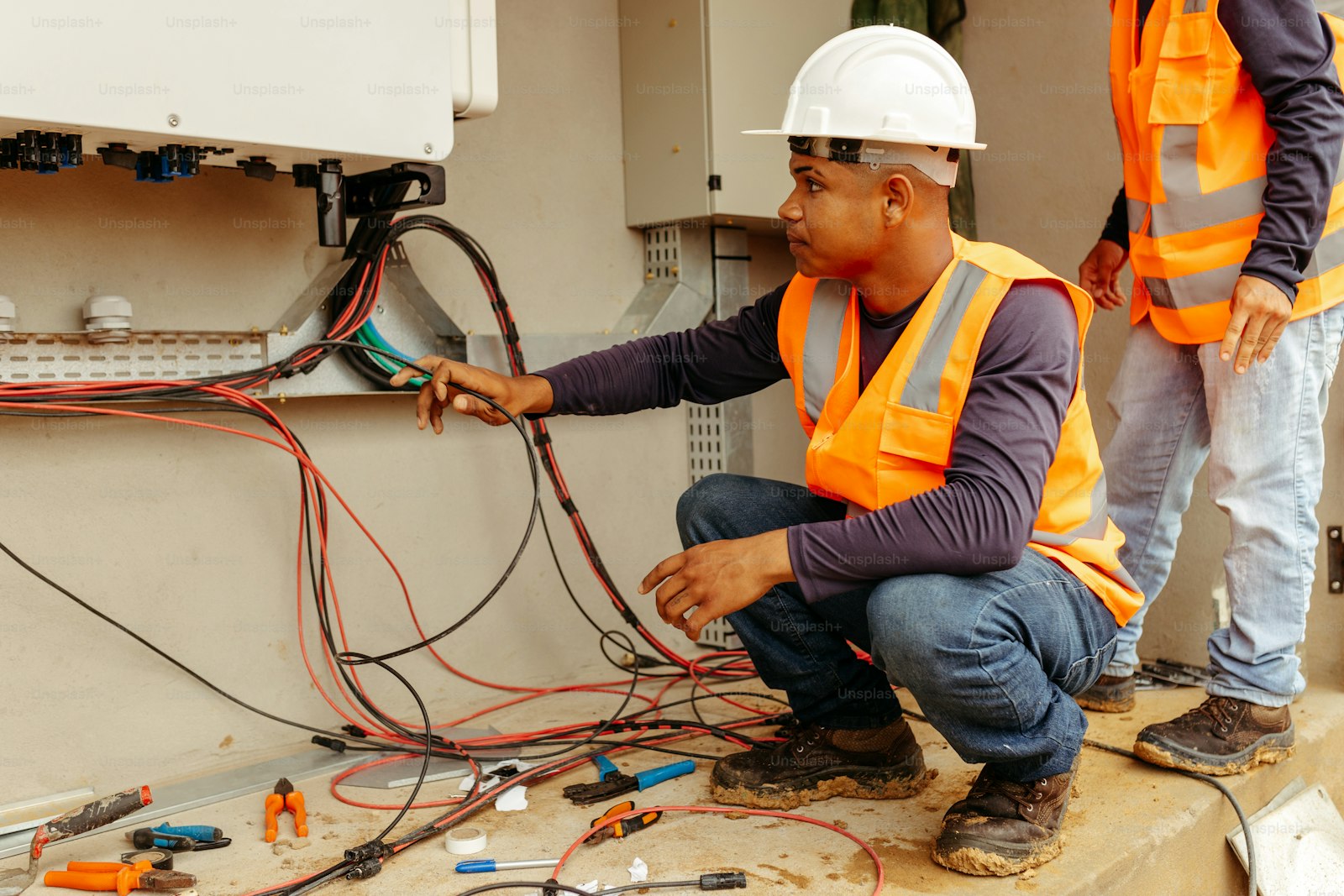Two licensed electricians in safety vests and hard hats working on electrical equipment