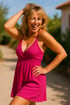 Lachende blonde Frau in einem pinkfarbenen Kleid mit Spaghettiträgern und einer Hand im Haar.
