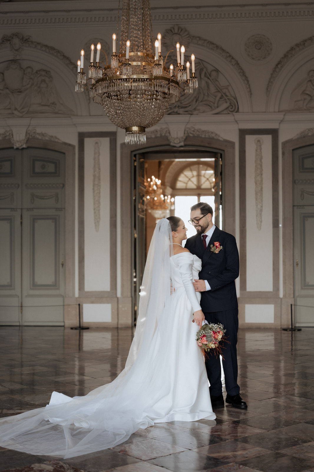 Brautpaar unter dem Kronleuchter, das Brautkleid mit langer Schleppe ausgebreitet, im Schloss Benrath in Düsseldorf.