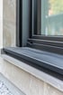 Detailansicht einer anthrazitfarbenen Außenfensterbank aus Aluminium an einem modernen Fenster mit Natursteinfassade – professionelle Montage durch den Fachbetrieb
