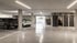 Helle Tiefgarage aus Sichtbeton mit markierten Parkplätzen, geparkten Autos, Fahrrädern und grauen Kellertüren.