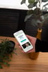 Hand hält Smartphone mit Website-Text „Lassen Sie Ihre Pflegesituation nicht dem Zufall überlassen“ neben einer Goldvase.