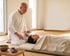 Ein Mann in weißer Kleidung gibt einer liegenden, zugedeckten Frau eine Shiatsu-Behandlung auf einer Bodenmatte.