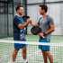 Zwei männliche Padel-Tennisspieler schütteln sich auf einem Padel-Platz die Hände, jeder hält einen Schläger.