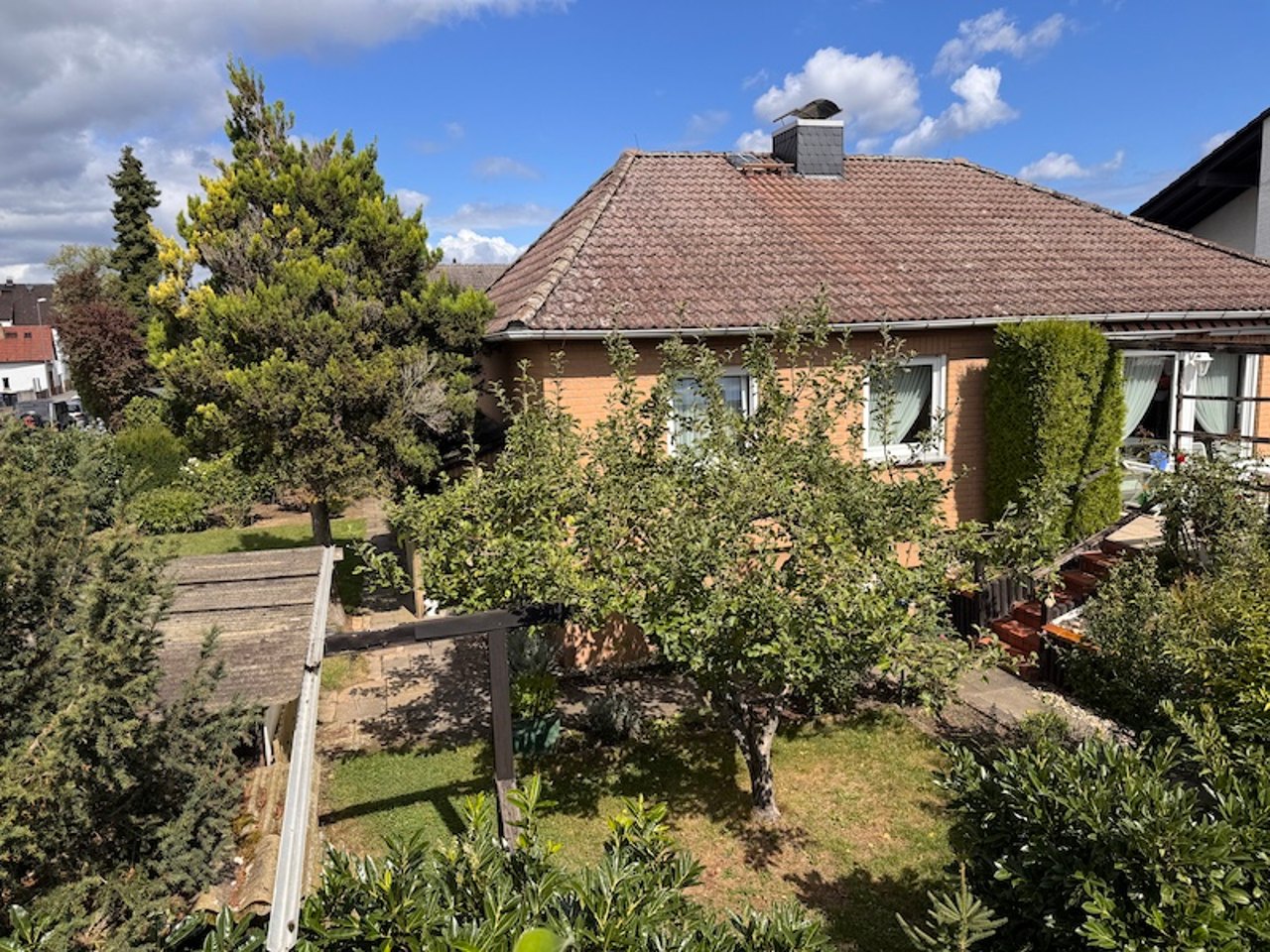Älteres Einfamilienhaus mit gewachsenem Garten und Terrasse an einem sonnigen Tag