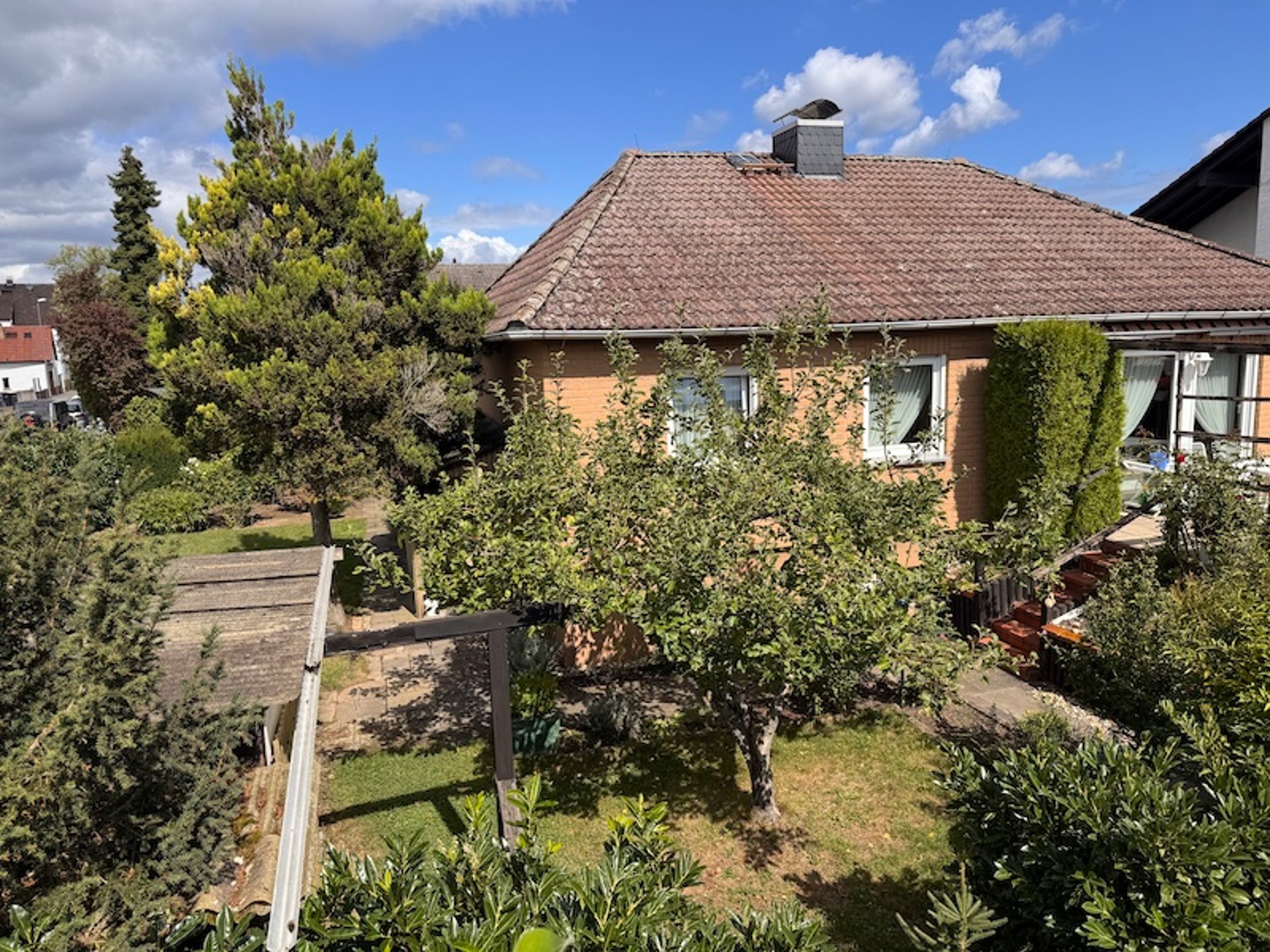 Älteres Einfamilienhaus mit gewachsenem Garten und Terrasse an einem sonnigen Tag