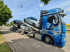 Blauer Autotransporter mit vier Pkws auf einem Seitenstreifen unter bewölktem Himmel.