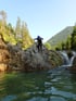 Person in Neoprenanzug springt von felsigem Ufer in klares Wasser.