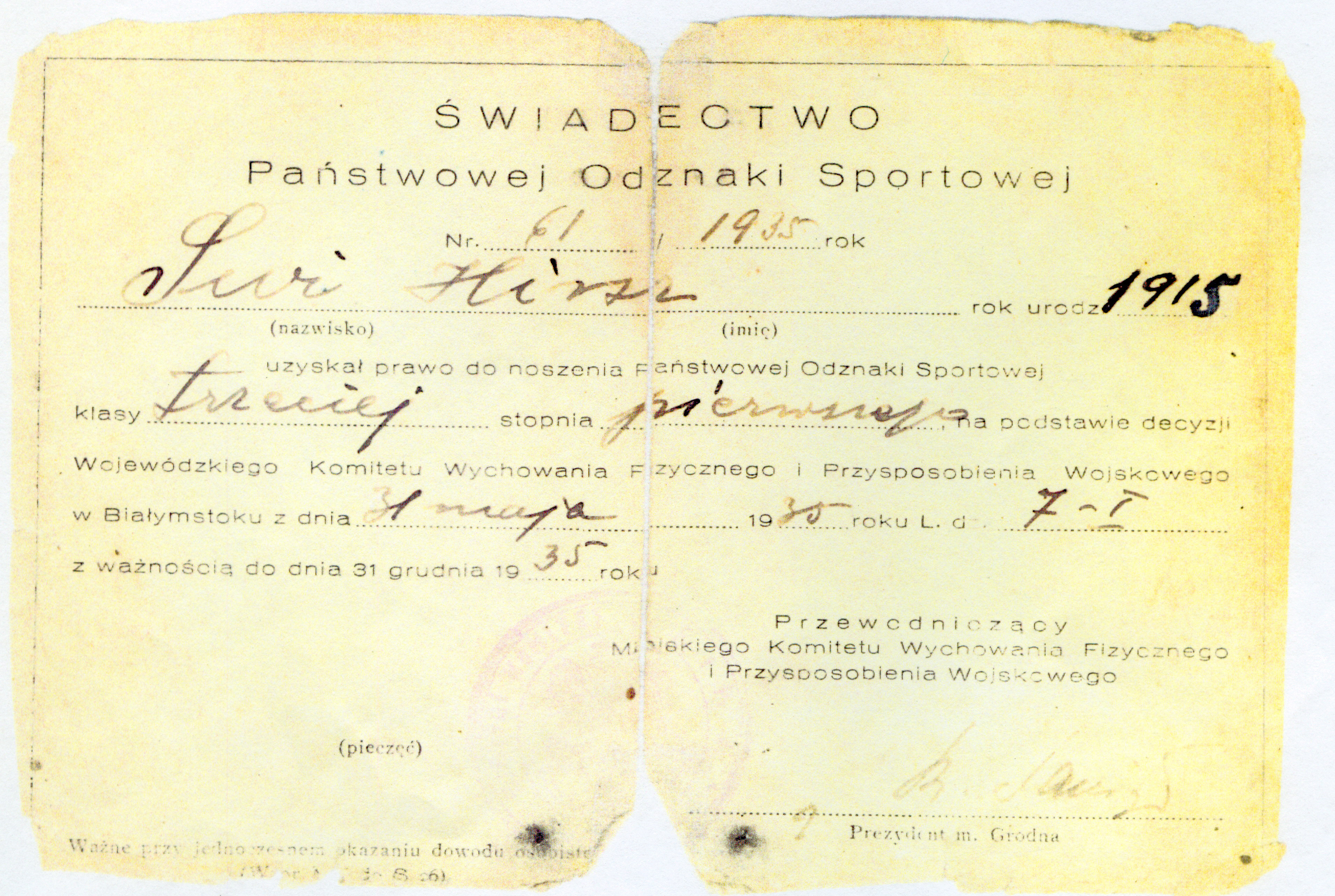 Świadectwo Państwowej Odznaki Sportowej Nº 61 de 1935 a nombre de Świ Hirsz, expedido por el Comité Provincial de Educación Física y Preparación Militar de Białystok. En la esquina superior derecha, sobre el campo «rok urodz.» (año de nacimiento), figura el año «1915» reescrito en tinta más oscura sobre la fecha original «1917».