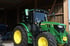 Grüner John Deere Traktor 6R-Serie mit gelben Felgen steht in einer Scheune.