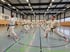 Gruppe von Karatekämpfern in weißen Anzügen und schwarzen Gürteln in einer Sporthalle, die eine Kampfhaltung einnehmen.