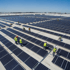 Arbeiter installieren Reihen von Solarmodulen auf einem großen Flachdach unter blauem Himmel.