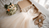 Hochzeitskleid in einem Karton, Brautschuhe und Brautstrauß auf einem weißen Bett.
