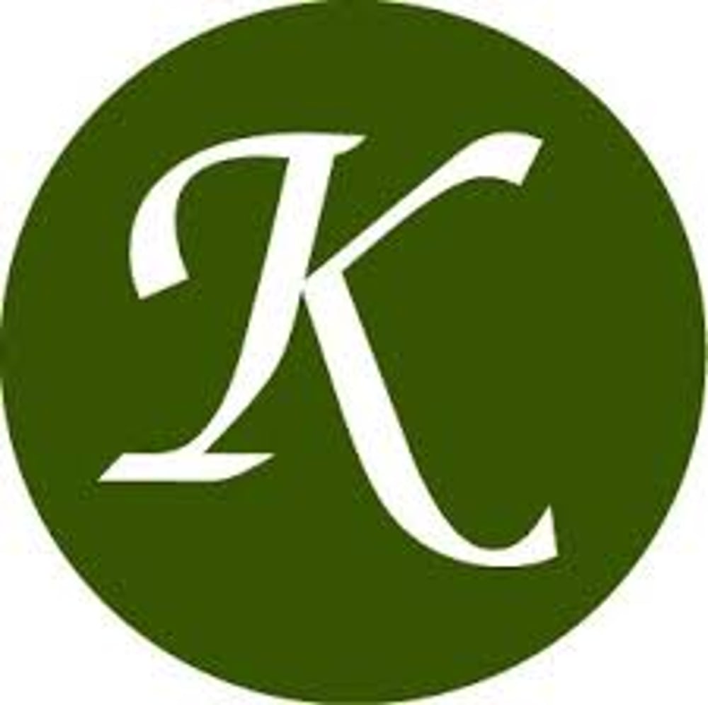 Weißer Großbuchstabe K in einer dekorativen Schriftart auf einem olivgrünen Kreis.