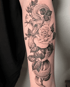 Schwarzes Tattoo auf einem Unterarm, das eine Schlange mit offenem Maul zeigt, die sich um Rosenblüten und Blätter windet.