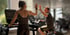 Zwei Personen geben sich im Fitnessstudio ein High Five, eine auf dem Laufband, die andere auf einem Heimtrainer.