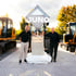 Zwei Männer stehen neben einem Juno-Logo-Denkmal mit der Aufschrift „since 1995“ vor gelben Baumaschinen.