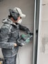 Bauarbeiter mit Staubmaske, Kappe und Gehörschutz bohrt mit Bohrmaschine in eine Wand.