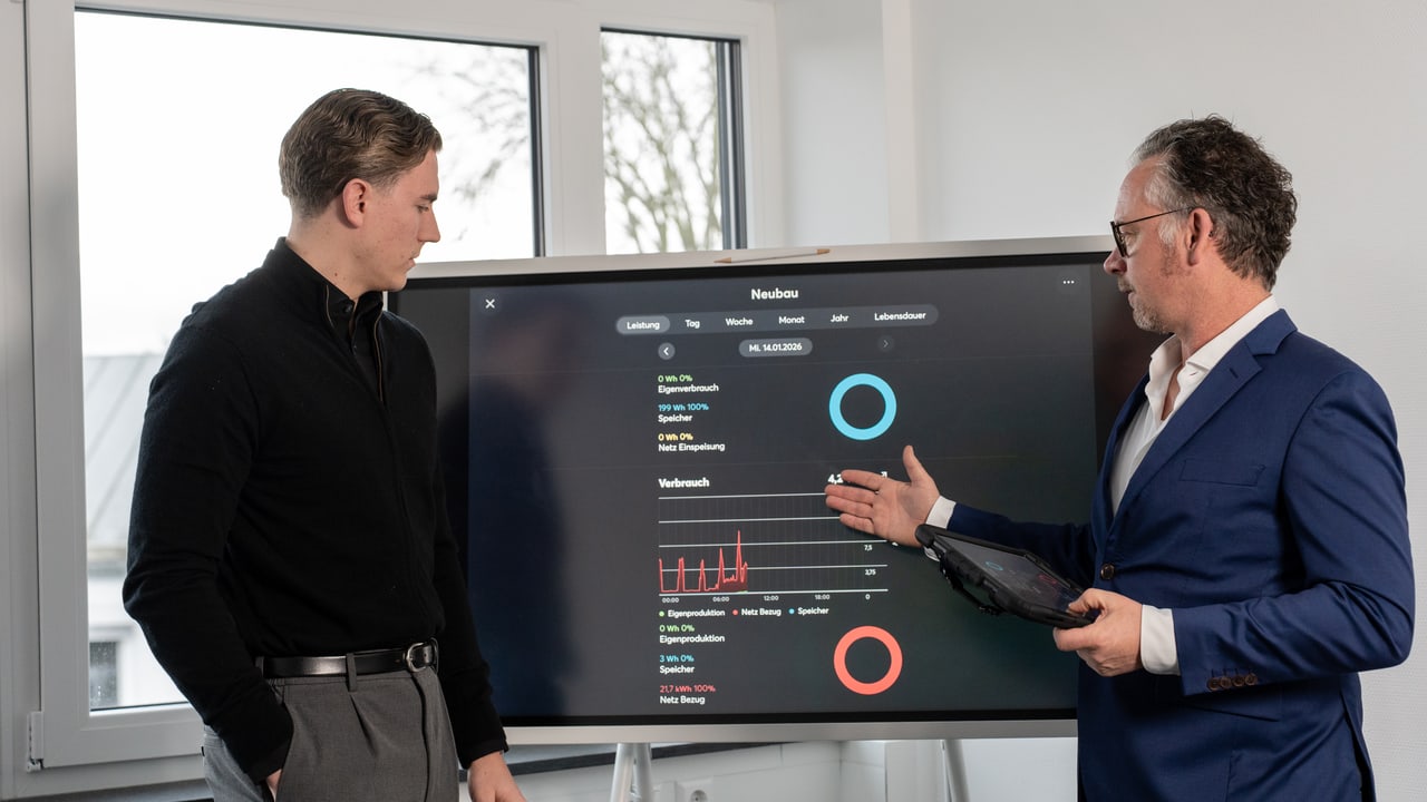Zwei Mitarbeiter besprechen Eigenverbrauch und Netzbezug am Monitoring-Display