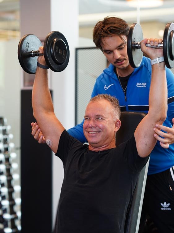 Mitglied trainiert mit Kurzhanteln unter Anleitung eines Trainers