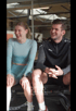 Zwei lachende Personen in Sportkleidung bei Pier 5 Training & Therapie sitzen auf einer Trainingsbank.