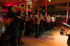 Audience members stand and clap in a dimly lit event space with red and pink lighting.