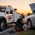 Towing Deltona roadside assistance technician changing a flat tire for a stranded vehicle on the roadside at sunset
