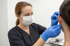 Eine Frau mit Maske und blauen Handschuhen untersucht das Ohr einer anderen Person.