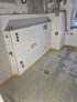 Badezimmer im Bau mit weißen Fliesenwänden, freiliegenden Rohren und "DURABASE ET-S" Fußboden.