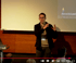Ein Mann mit Brille und dunklem Sakko gestikuliert vor einer Leinwand mit einer Präsentation.