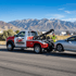 Towing Sandy wheel lift towing service loading a sedan onto a tow truck along a roadway with a tow operator securing the vehicle.