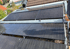 Sechs Reihen schwarzer Solarmodule auf einem Flachdach, umgeben von Kies und einem Hausdach im Hintergrund.