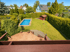 Hinterhof mit blauem Pool, Rasen, Terrasse und Gartenhaus, umgeben von Hecken und Bäumen.