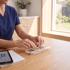 A person in blue scrubs organizes various pills into a clear plastic daily pill organizer on a wooden table.