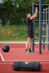 Mann in Sportkleidung befestigt ein TRX-Band an einer Turnstange, daneben ein 8-kg-Medizinball.