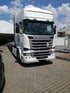 Weißer Scania R 490 LKW mit Sattelauflieger parkt auf gepflastertem Firmengelände unter blauem Himmel.
