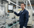 Ein Mann in blauer Arbeitskleidung und Schutzbrille lächelt neben einer CNC-Maschine.