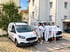 Vier Handwerker in weißer Arbeitskleidung stehen lächelnd zwischen zwei weißen Ford-Firmenwagen vor einem Wohnhaus.