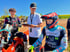 Drei Motocross-Fahrer, zwei in voller Rennmontur, einer mit Helm, auf einer Dirtbike-Strecke.