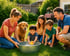 Lachende Familie mit Hund im Garten beobachtet ein Kleinkind, das mit einer Quietscheente in einer Zinkwanne spielt.