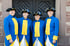 Vier lächelnde Personen in blau-gelben historischen Uniformen mit Dreispitz-Hüten vor einer dunklen Holztür.