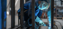 Ein Schweißer in Schutzkleidung beugt sich über ein Metallstück und erzeugt blaue Funken.