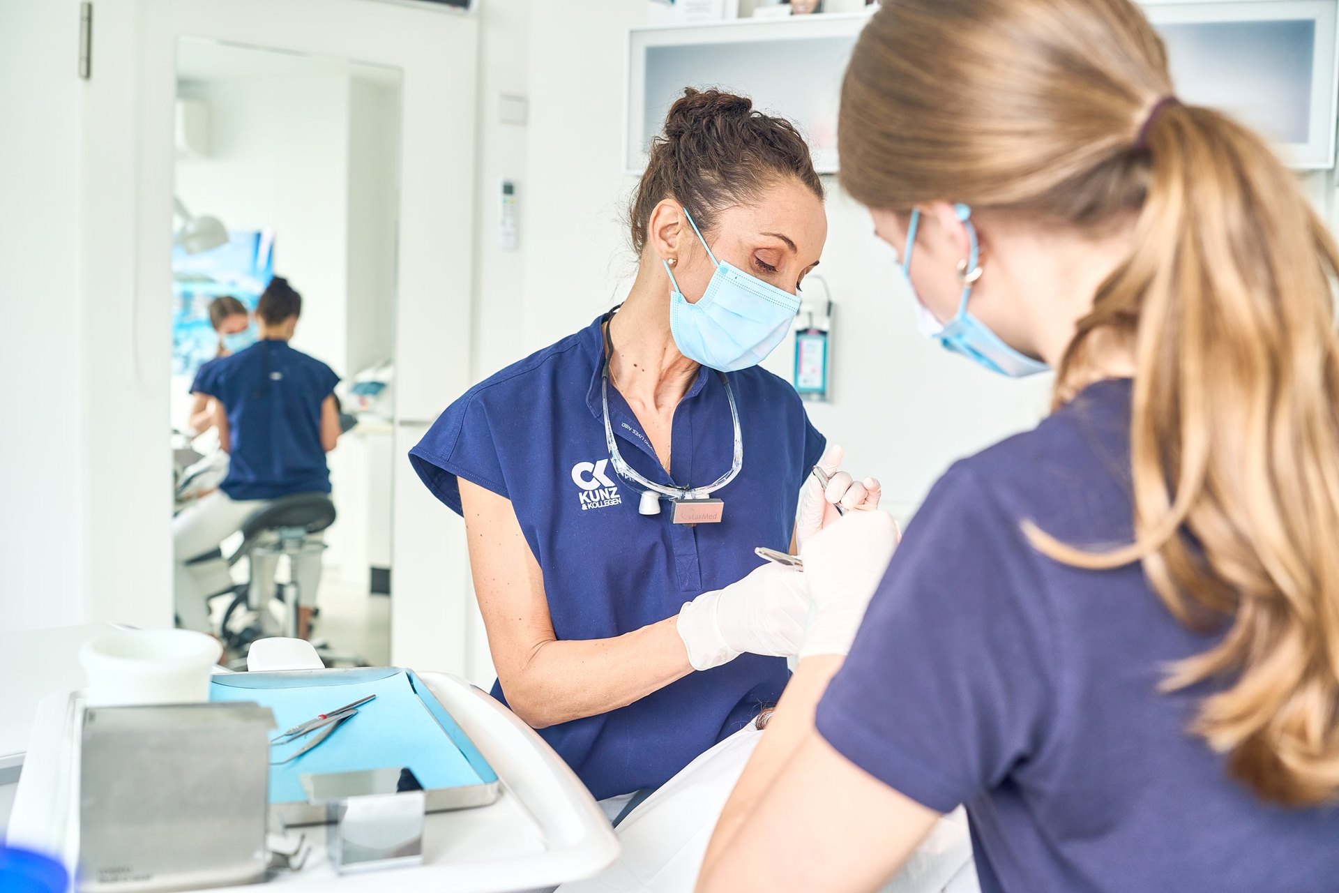 Dr. Carolin Kunz mit Lupenbrille bei der Behandlung, mit Assistenz
