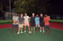 Sieben Personen stehen abends nebeneinander auf einem Sportplatz, einer hält einen Volleyball